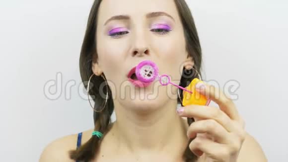 粉妆少女的肖像正在吹肥皂泡滑稽的微笑女性吹肥皂泡白色背景视频的预览图