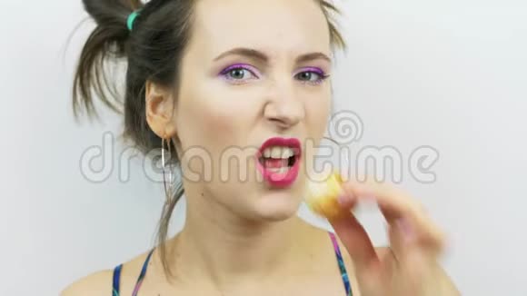 开朗的黑发女孩在镜头前在白色背景下吃普通话微笑的年轻女子粉唇吃橙色的摄影师视频的预览图