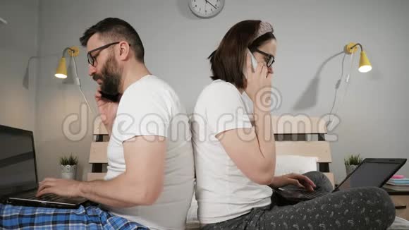 在家工作自由职业概念夫妻俩坐在卧室的床上背靠背一边工作一边打字视频的预览图