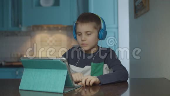 自闭症男孩在厨房里用带耳机的平板电脑有自闭症的孩子在家里四处张望自闭症视频的预览图