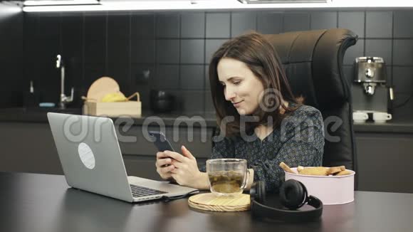 年轻女性在家工作使用笔记本电脑在智能手机上输入信息女性自由职业者在家厨房工作视频的预览图