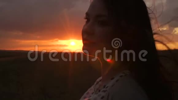 留着长发的女孩的剪影站在夕阳下的田野里视频的预览图