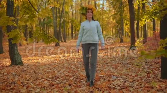 动作缓慢美丽的女人头上有枫叶的呼吸穿过秋天的森林看着树视频的预览图