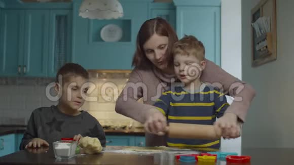 年轻的母亲和两个儿子烹饪不同形状的面团孩子们帮妈妈在家蓝厨房做糖果视频的预览图