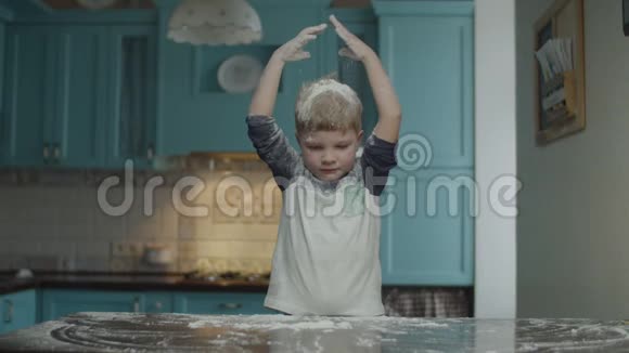金发的学龄前儿童在蓝色的厨房里玩面粉男孩在桌上玩面粉孩子洒在他头上视频的预览图