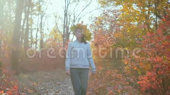 美丽的女人秋天的树叶在森林的头上漫步视频的预览图