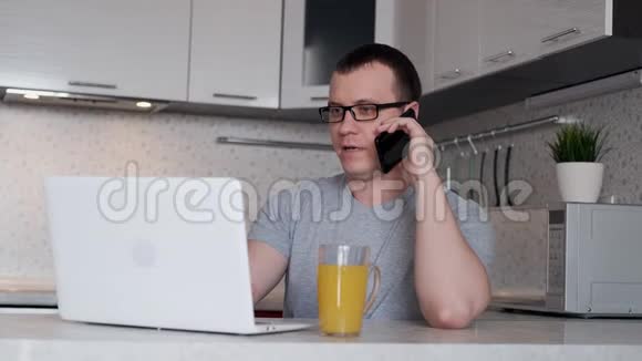 一个男人在一个远程工作期间从家里讲电话和看手提电脑屏幕而坐在一张桌子视频的预览图