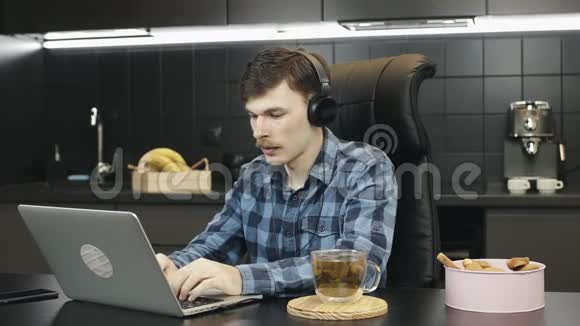 男性耳机自由职业者在家工作一个人在家里坐在厨房里用笔记本电脑在网上工作的人视频的预览图