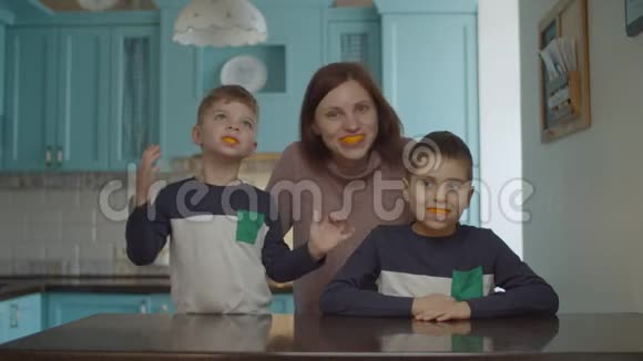 有趣的一家人在嘴里玩橘子皮微笑的女人和孩子嘴里有橘子水果橙色的微笑视频的预览图