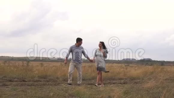 幸福的怀孕家庭在日落时分漫步在田野一个男人牵着妻子的手视频的预览图