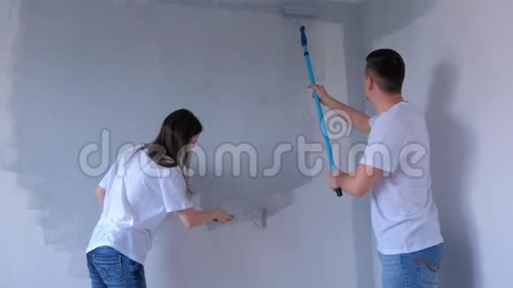 画家们年轻的男女正在用油漆辊画灰色的墙壁视频的预览图