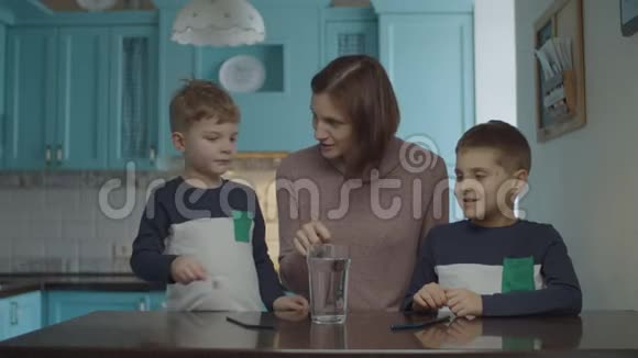年轻的母亲和两个孩子在厨房里做自制的苏打水饮料孩子们喝着泡泡饮料视频的预览图