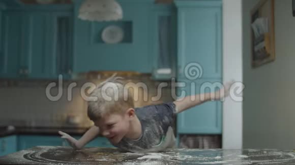 金发的学龄前儿童在蓝色的厨房里玩面粉男孩在桌上玩面粉孩子假装是飞机视频的预览图