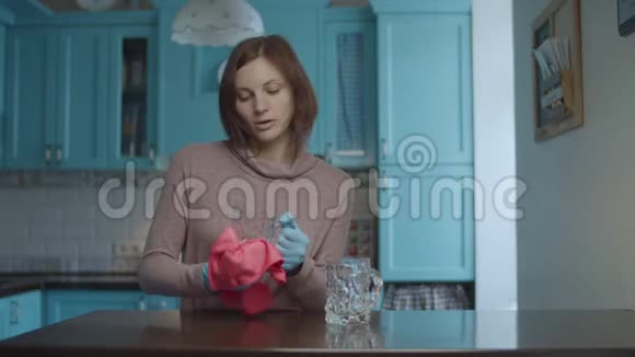年轻的微笑着30多岁的女性戴着手套用粉红色的餐巾擦玻璃杯在蓝色的厨房里跳舞女人快乐视频的预览图
