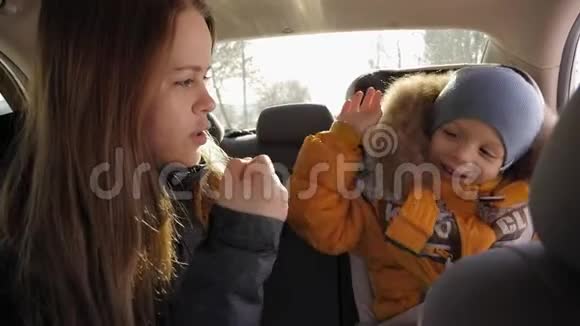 一个快乐的妈妈带着一个小孩子玩得开心在后座的车里玩视频的预览图