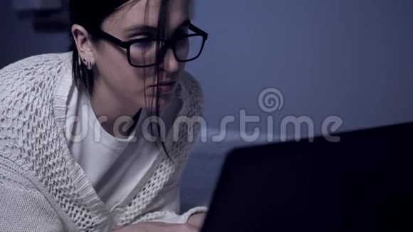 女孩晚上在笔记本电脑上工作漂亮的女学生黑客或戴眼镜的自由职业者躺在床上视频的预览图
