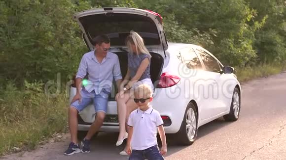 一个小男孩站在靠近汽车的路上他的父母坐在后备箱里视频的预览图