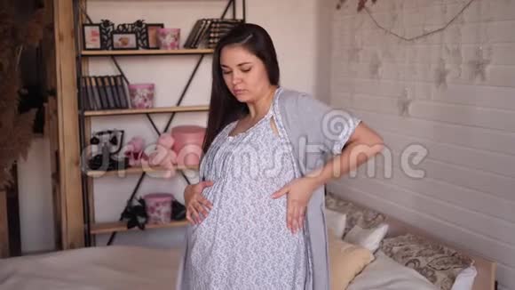在卧室里有胃痛或背痛的悲伤孕妇穿着睡衣视频的预览图