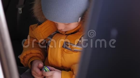 一个悲伤的男孩坐在一个孩子的座冬天带着一个小球的肖像视频的预览图