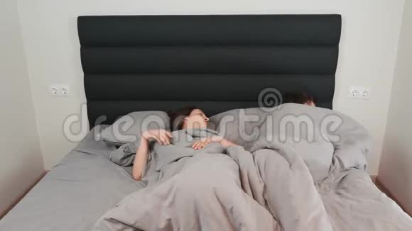 男女夫妇躺在床上放松的时间推移一对白人年轻夫妇在家里躺在灰色的床上视频的预览图