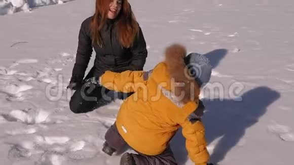 冬天妈妈带着一个小儿子在白雪覆盖的公园里玩耍他们扔雪视频的预览图