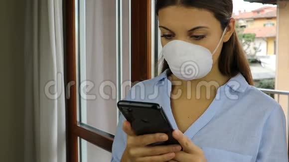 COVID19大流行冠状病毒女性家庭隔离自动隔离带带智能手机面罩阅读信息视频的预览图