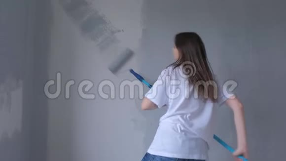 年轻的女画家正在用油漆滚筒和舞蹈用灰色油漆墙壁视频的预览图