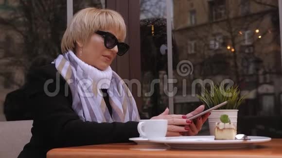 一位年长的商务女士坐在一家带咖啡和平板电脑的街头咖啡馆里视频的预览图