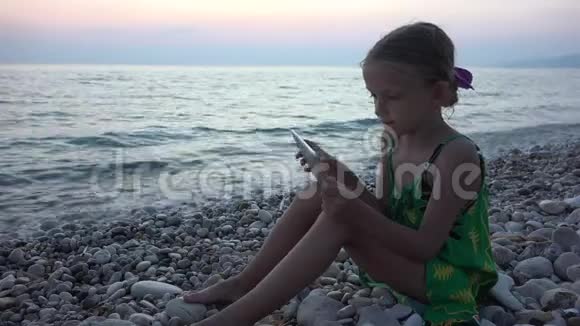 4K小子在海滩上玩平板电脑日落时在海滨的孩子海边的少女嬉戏视频的预览图