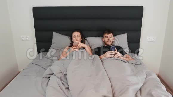 女性和男性躺在卧室里看着他们的智能手机关系危机关系方面的困难年轻的妈妈视频的预览图