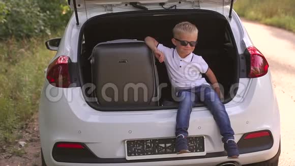 小男孩戴着太阳镜坐在后备箱里提着手提箱然后离开视频的预览图