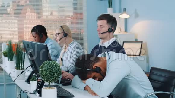 混合种族的客户支持接线员在呼叫中心的桌子上睡着了视频的预览图