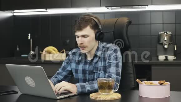 戴着耳机听音乐和在家里用笔记本电脑工作的人快乐的男人在家工作青年男性自由职业者视频的预览图