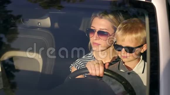 一位年轻的母亲和她的儿子戴着太阳镜在夕阳下的汽车上的肖像视频的预览图
