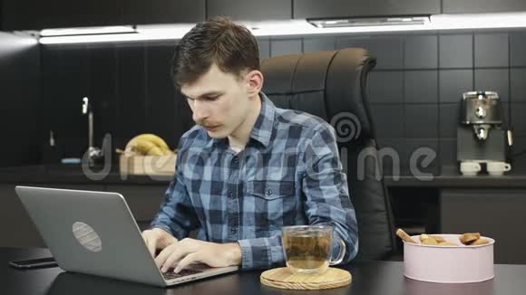 年轻人在家里用笔记本电脑工作商人在厨房里用笔记本电脑的肖像男性自由职业者用键盘打字视频的预览图