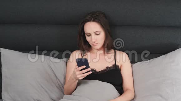 年轻的黑发女人在客厅里躺在床上看智能手机屏幕的肖像白人女性在手机屏幕上打字视频的预览图