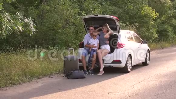 有儿子的父母坐在空路上的汽车后备箱里家人在度假视频的预览图