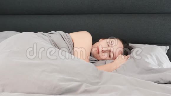 布鲁内特迷人的女性独自躺在床上女人早上在家里的灰色床上醒来年轻女孩躺在床上微笑视频的预览图