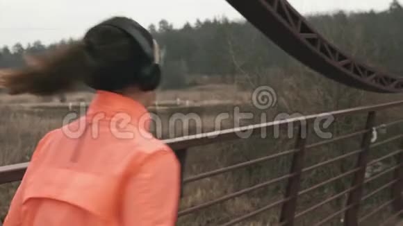 深色头发的女人戴着耳机在桥上奔跑性感的女运动员户外训练年轻运动员跑步视频的预览图