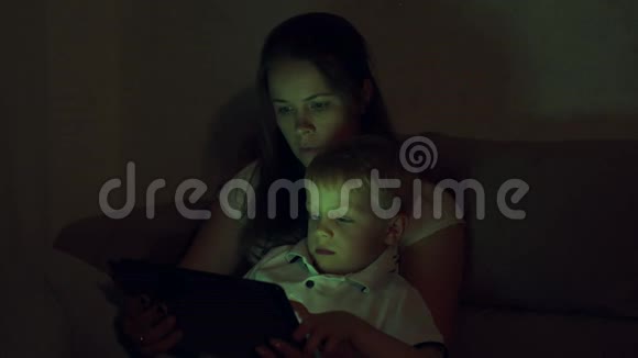 一幅母亲和儿子在黑暗中带着平板电脑在家里的肖像视频的预览图