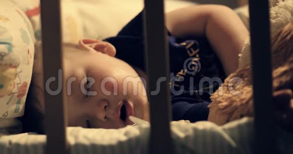 婴儿在睡觉可爱的孩子晚上睡在婴儿床上灯发出的暖光落在床上特写视频的预览图