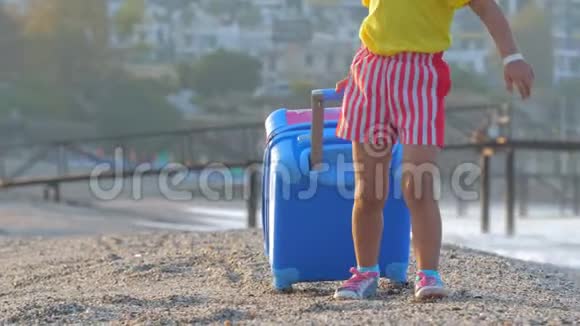 小可爱微笑的女孩正拿着一个手提箱在度假海滩上散步视频的预览图
