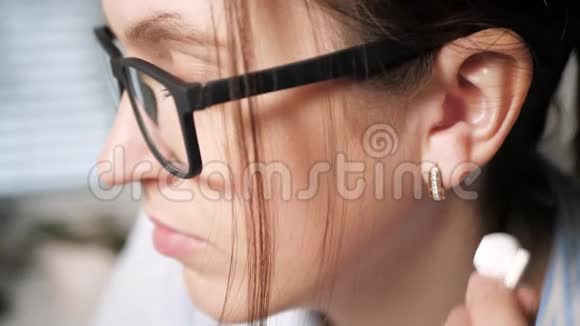 戴眼镜的年轻女孩左耳戴白色耳机听音乐的概念特写慢动作视频的预览图