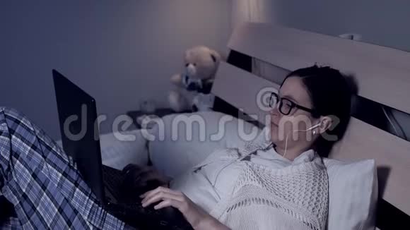 晚上带笔记本电脑的女孩有魅力的年轻女学生或自由职业者躺在床上在笔记本电脑上打字视频的预览图