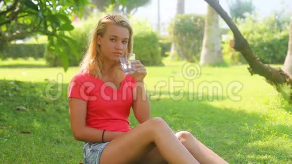 年轻漂亮的女孩坐在树荫下喝水视频的预览图