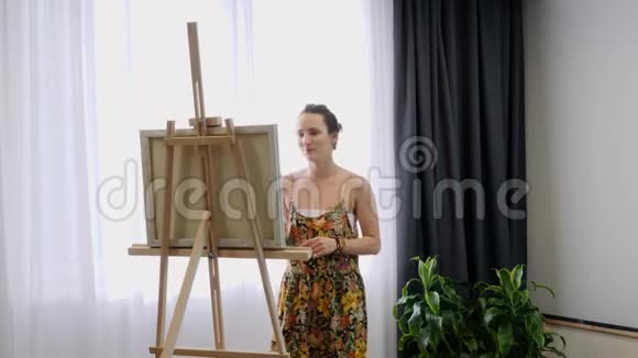年轻有才华的女人在艺术之家画画布女艺术家站在画架附近画在画布上内部资料视频的预览图