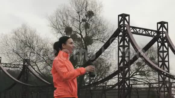 活泼的女运动员穿着鲜艳的运动服从瓶子里喝水年轻的黑发女人在跑步时喝水视频的预览图