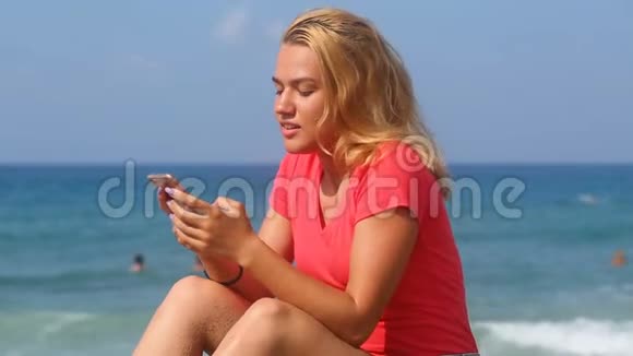 年轻漂亮的女孩在大海的背景上读短信视频的预览图