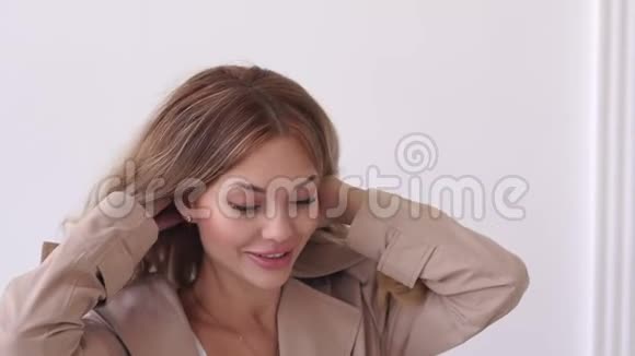一个穿米色外套的年轻女孩在工作室的白色背景上的特写视频的预览图