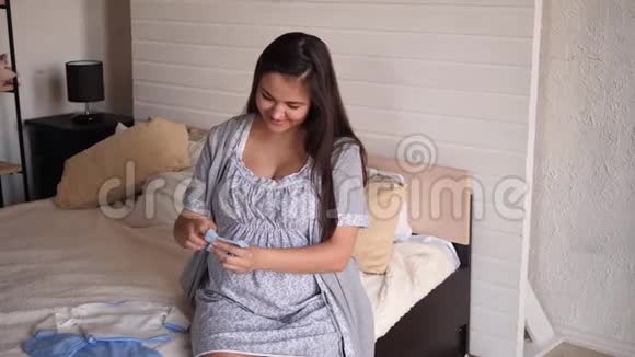 有孩子衣服的孕妇坐在卧室的床上视频的预览图